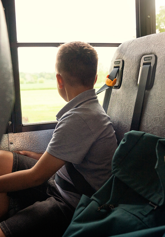 A child sitting on a school bus with a seat belt on