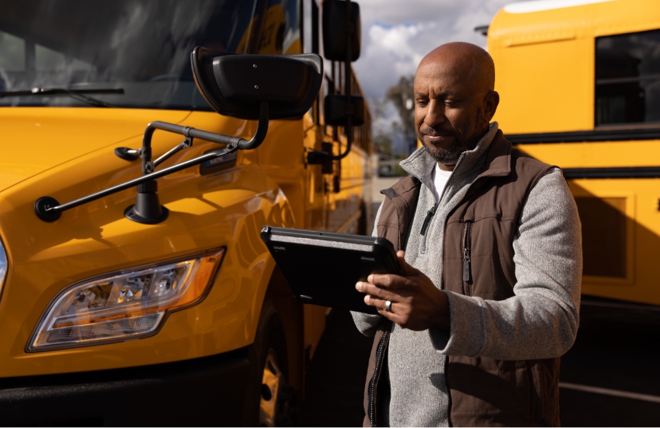 Man on tablet in front of school bus